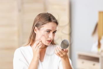 Portrait of young woman with acne problem looking in mirror at home�