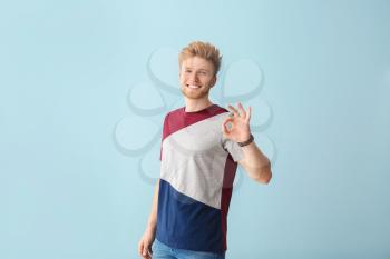 Portrait of young man showing OK gesture on color background�