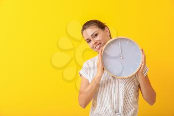 Beautiful young woman with clock on color background�