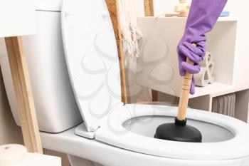 Man using plunger to unclog a toilet bowl�