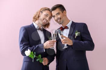 Happy gay couple with champagne on their wedding day against color background�