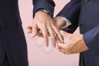 Happy gay couple exchanging rings on their wedding day against color background, closeup�