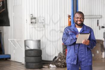 African-American mechanic with tablet computer in car service center�