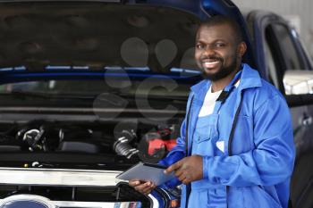 African-American mechanic with tablet computer working in car service center�
