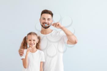 Portrait of father and his little daughter brushing teeth on light background�