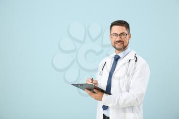 Portrait of male doctor with clipboard on color background�