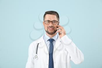Portrait of male doctor talking by phone on color background�