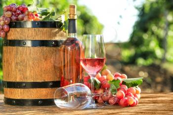 Glasses and bottle of wine with fresh grapes and barrel on wooden table in vineyard�