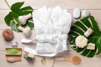 Clean bathrobe with spa supplies on wooden background�