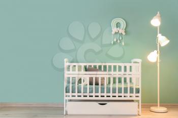 Stylish baby bed with lamp near color wall in interior of children's room�