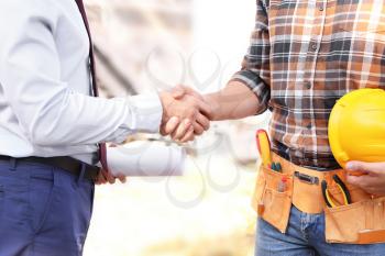 Male architect and builder shaking hands outdoors�