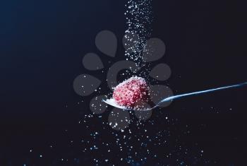 Sprinkling of sugar into spoon with fresh strawberry against dark background�