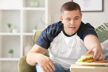 Overweight man eating unhealthy food at home�