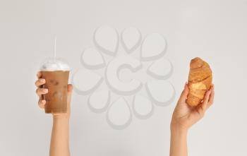 Female hands with cup of tasty frappe coffee and croissant on light background�
