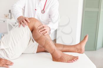 Doctor examining mature man with joint pain in clinic�