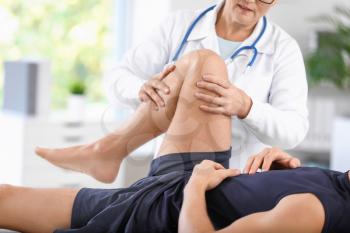Mature doctor examining sportsman with joint pain in clinic�