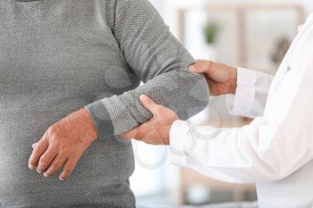 Doctor examining mature man with joint pain at home, closeup�