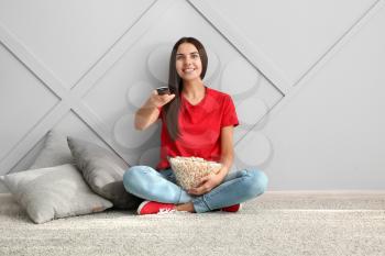 Young woman with popcorn watching movie near grey wall�