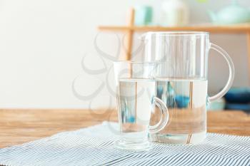 Glass cup and jug of fresh water on table indoors�