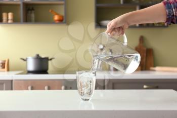 Woman pouring fresh water from jug into glass on table�