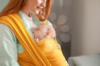 Young mother with little baby in sling at home�