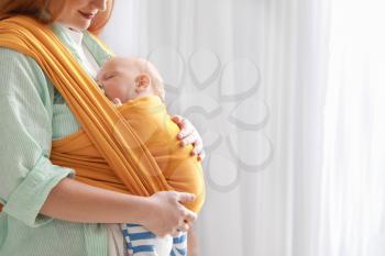 Young mother with little baby in sling at home 