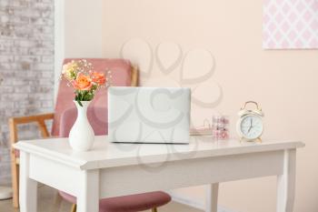 Beautiful bouquet in vase and laptop on table in room�