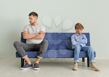 Quarreled father and son sitting on sofa at home�