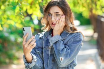 Surprised young woman with mobile phone outdoors�