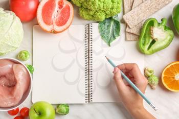 Woman writing something in notebook and healthy products on white table. Diet concept�
