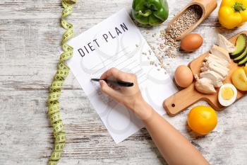 Woman writing something on sheet of paper with diet plan, top view�