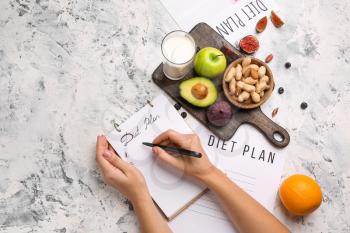 Woman writing something in notebook and healthy products on white table. Diet concept�