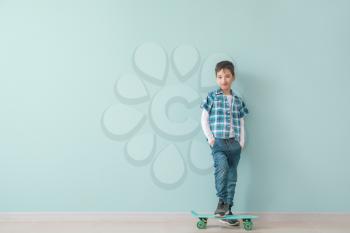Cute fashionable boy with skateboard against color wall�