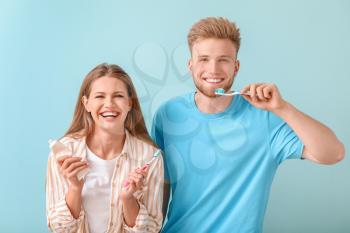 Young couple brushing teeth on color background�