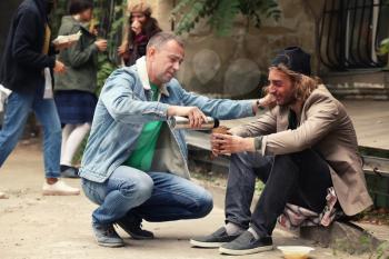 Volunteer giving drink to homeless man outdoors�