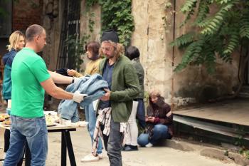 Volunteers giving clothes and food to homeless people outdoors�