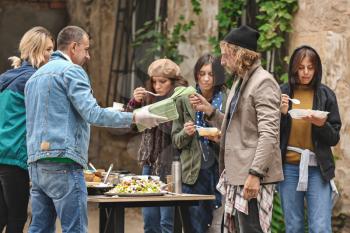 Volunteers giving food to homeless people outdoors�