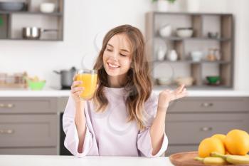 Beautiful young woman drinking orange juice in kitchen�