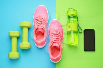 Sports water bottle, shoes, mobile phone and dumbbells on color background�