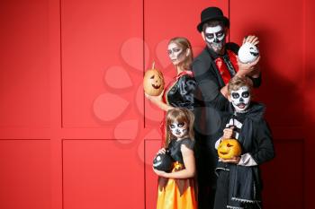 Family in Halloween costumes and with pumpkins on color background�