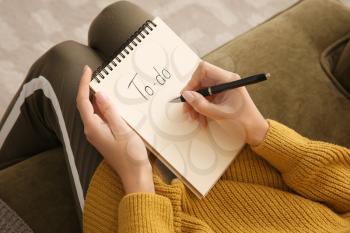 Woman making to-do list while sitting on sofa, closeup�