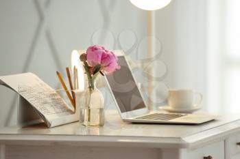 Vase with beautiful flowers and laptop on table in room�