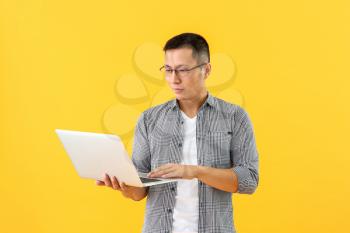 Male Asian programmer with laptop on color background�