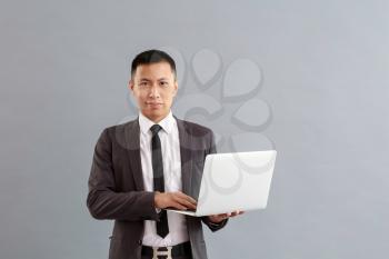 Asian businessman with laptop on grey background�