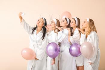 Beautiful young women in bathrobes and with air balloons taking selfie on light background�