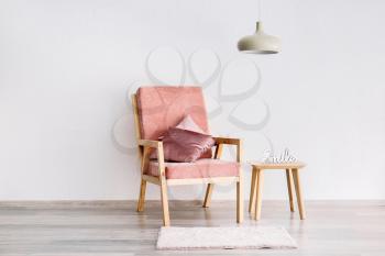 Stylish armchair with table and lamp near white wall�
