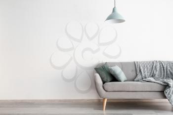 Stylish sofa with lamp near white wall�