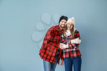 Happy young couple in warm winter clothes on color background�