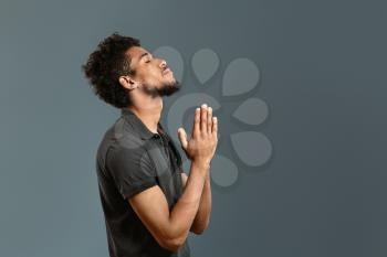 Portrait of African-American man praying against grey background�