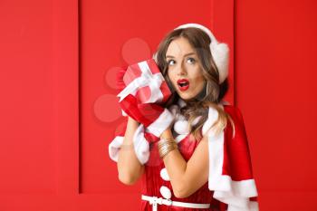 Surprised woman dressed as Santa with gift on color background�